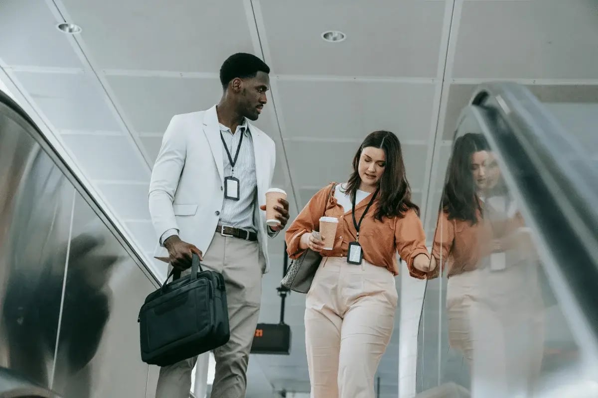 Colleagues with coffee cups discussing work on escalator.