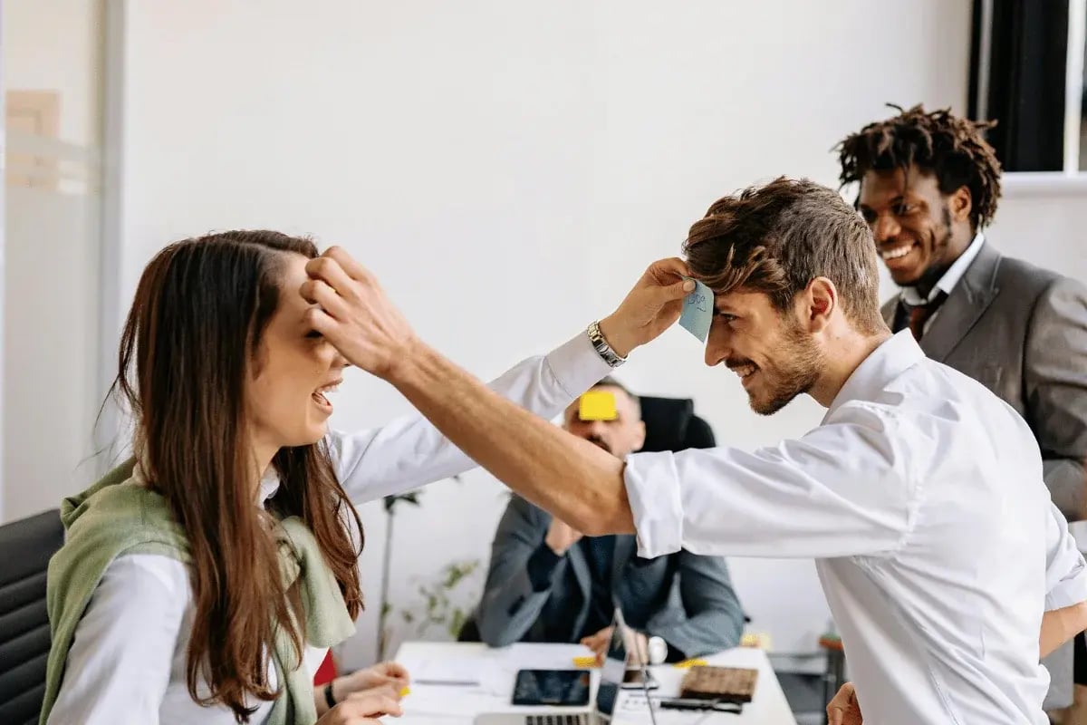 Coworkers laughing and playing a sticky note guessing game in a fun office team-building activity.