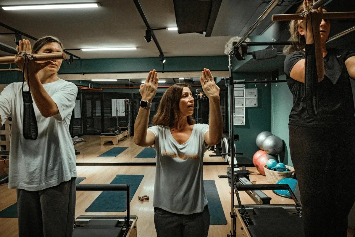 Fitness trainer coaching two women during pilates class.