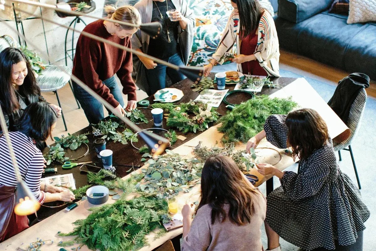 A group of women crafting wreaths with greenery at a collaborative DIY event.