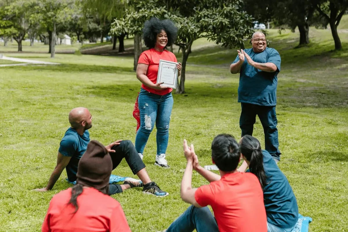 Team celebrating outdoors as a woman receives a certificate of achievement.