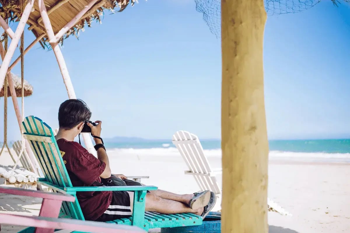 Man relaxing on a beach chair while looking through binoculars.