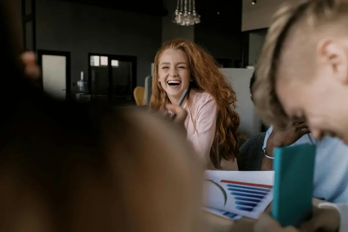 Team meeting with colleagues laughing together while reviewing charts and documents in a modern office setting.