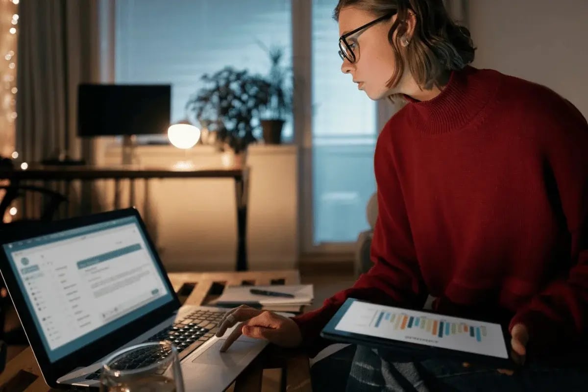A woman reviewing digital analytics on a tablet while managing emails on her laptop.