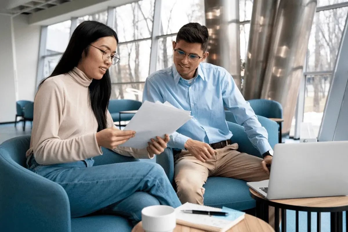 Two colleagues reviewing documents together in a well-lit workspace with a laptop nearby.