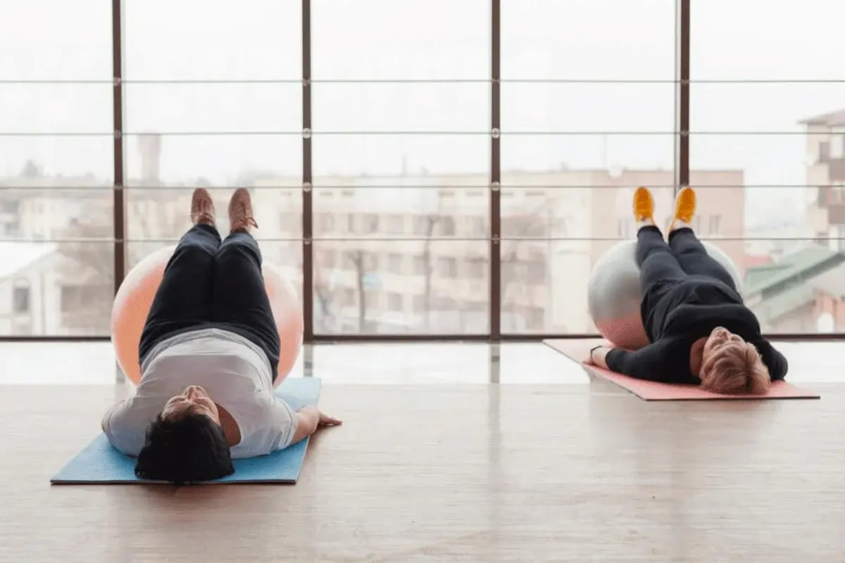 Two individuals performing a fitness routine using stability balls in a gym.