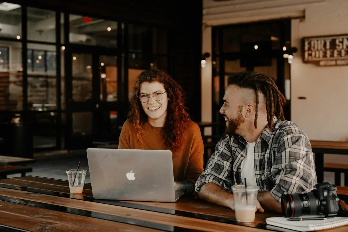 Two friends working on laptop together at coffee shop.