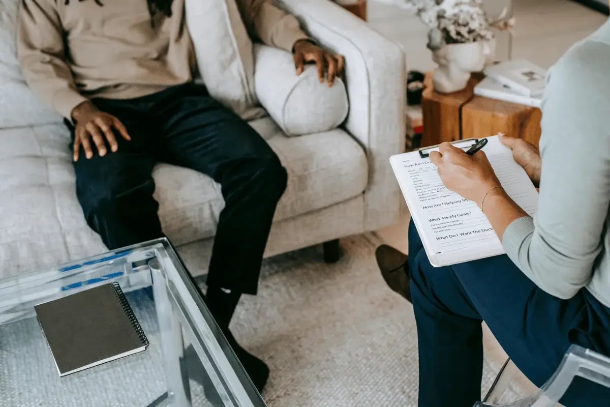 A person taking notes during a conversation with another person in a cozy living room setting.
