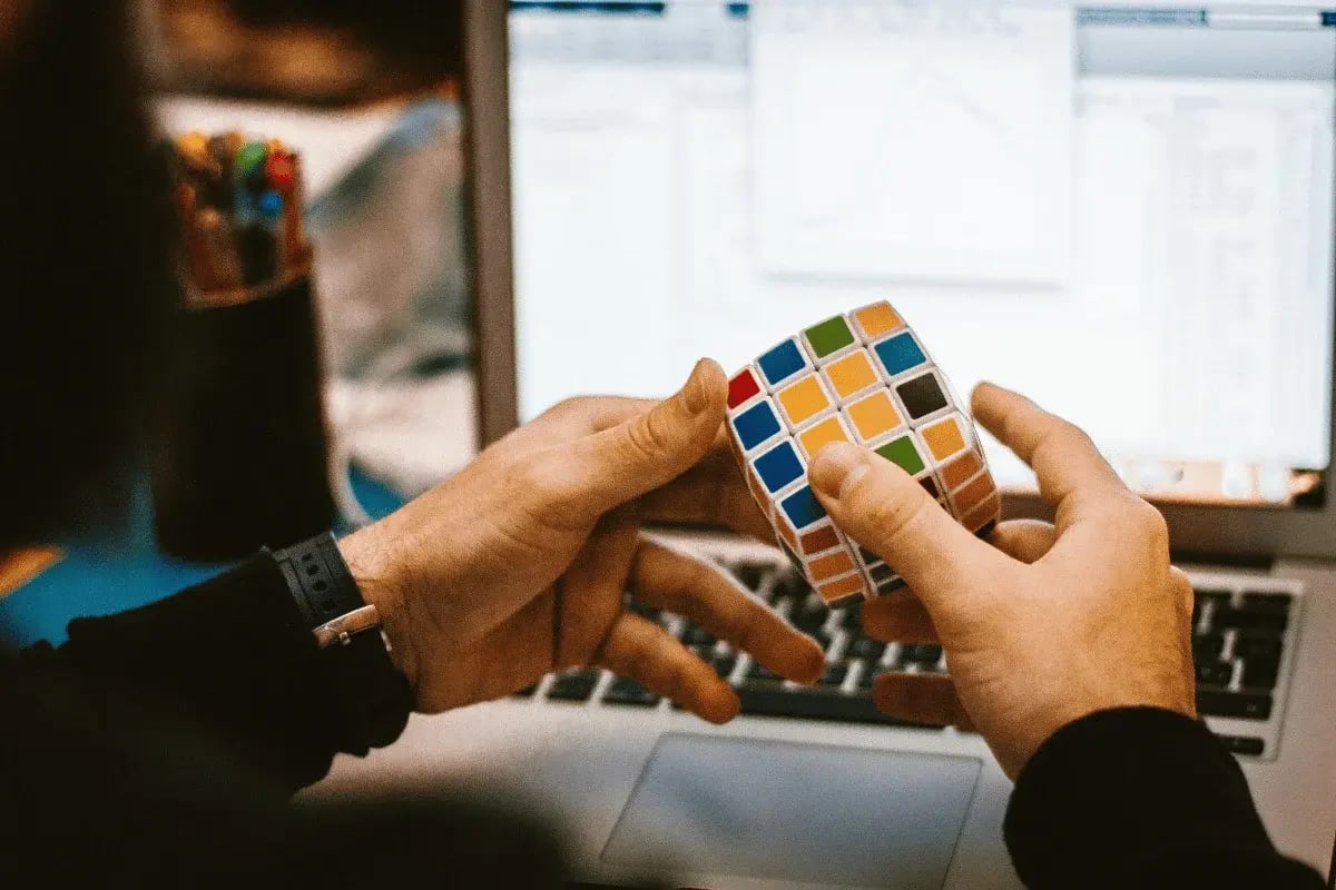 Hands solving a Rubik's Cube in front of a laptop.