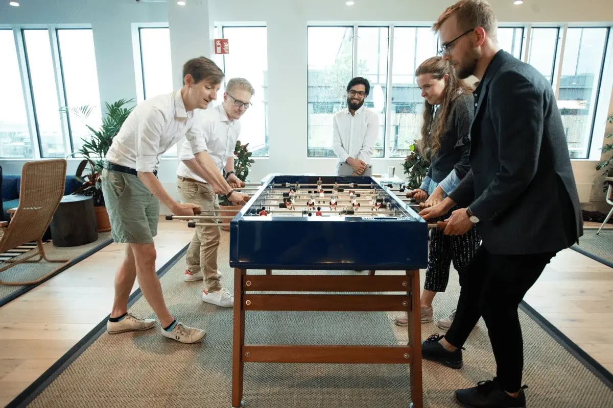 Group of coworkers playing foosball in modern office lounge.