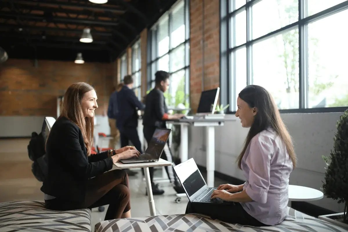 Two professionals working on laptops in a modern office space, engaged in a collaborative environment.