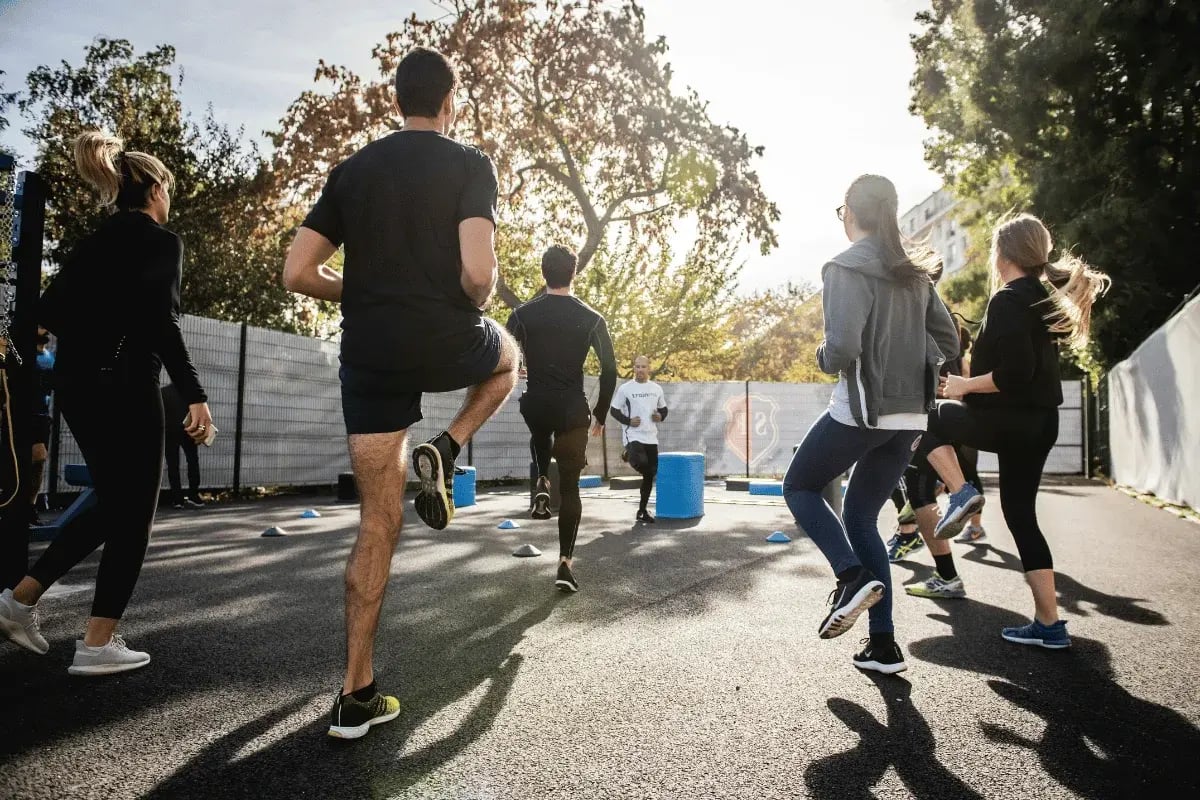 A group of people participating in an outdoor workout, following a trainer's instructions.