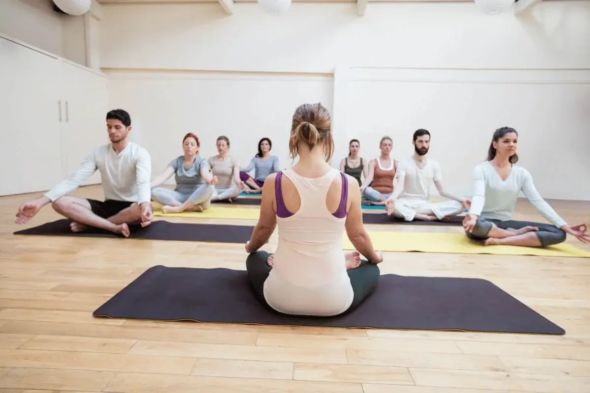 A group of people meditating in a yoga studio, practicing mindfulness on mats in a bright, peaceful environment.