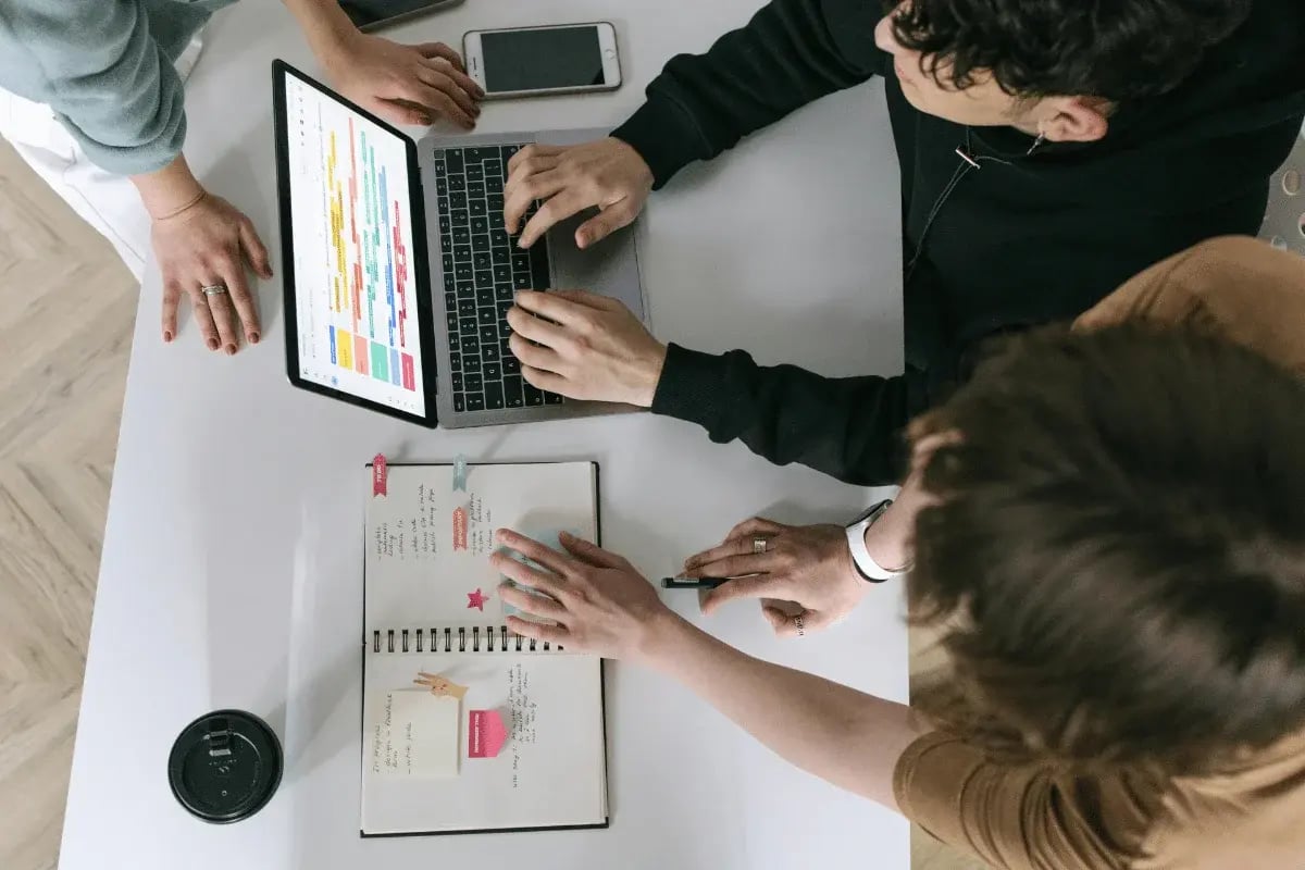 Team collaborating around a table with a laptop, tablet, and notebook.