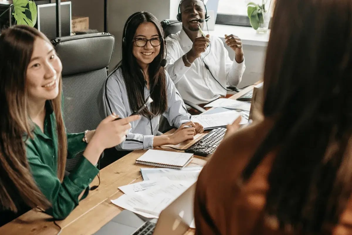 Diverse call center staff smiling and collaborating at their desks.