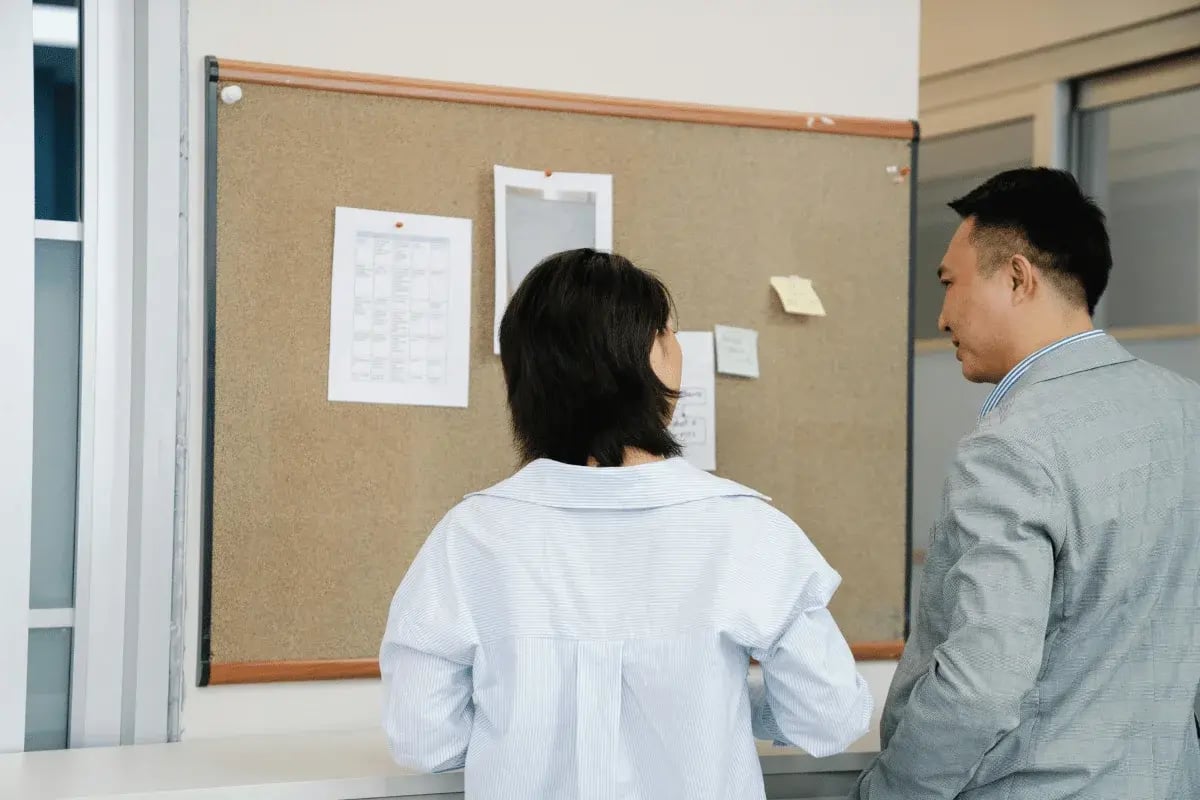 Office employees reviewing notes posted on a cork bulletin board.