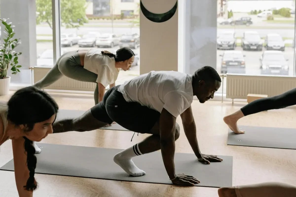 A man and woman practicing yoga in a studio, with the man performing a mountain climber pose.