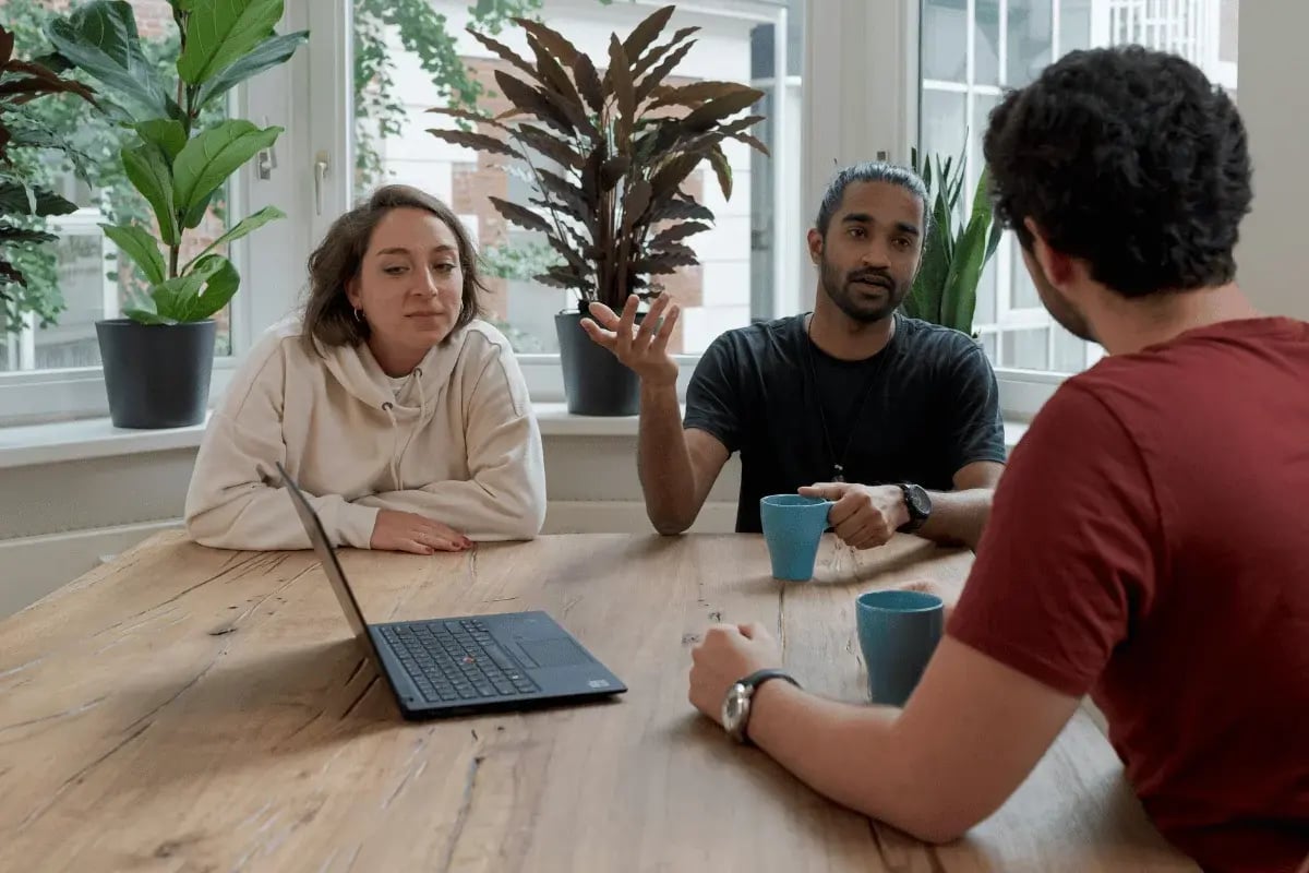 Team meeting with three colleagues at wooden table.