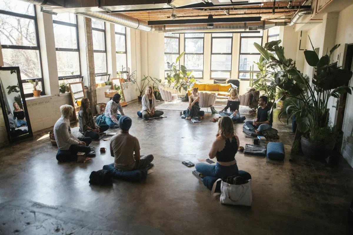Group meditation session in a sunlit urban studio with indoor plants.