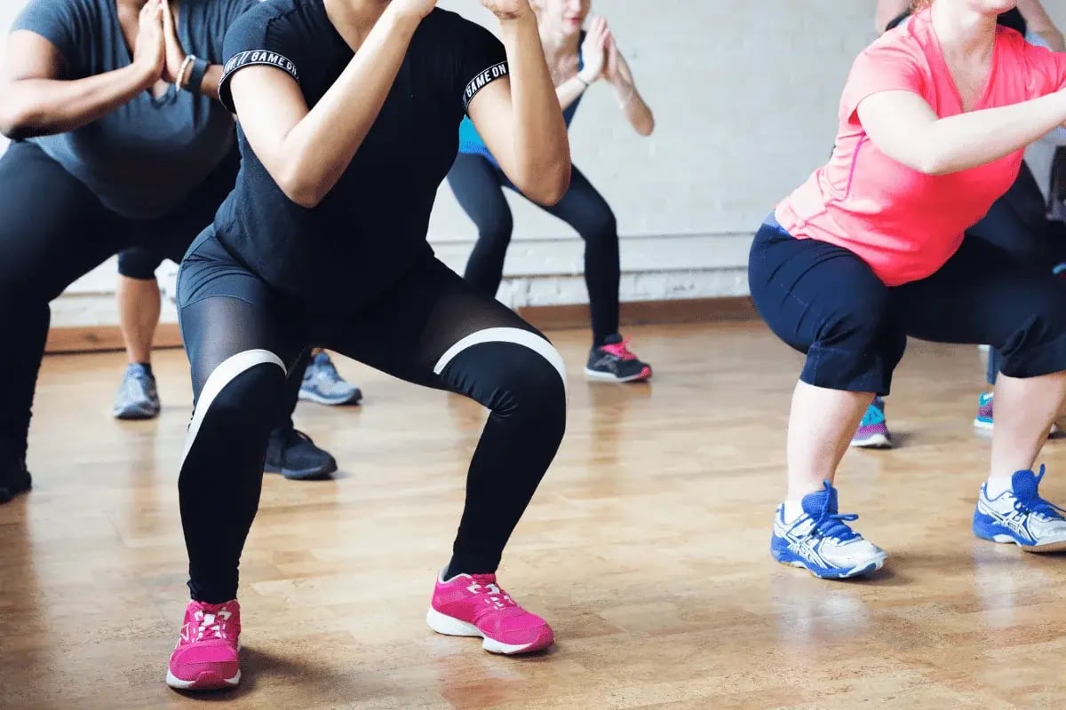 Group fitness class doing squats on hardwood floor.