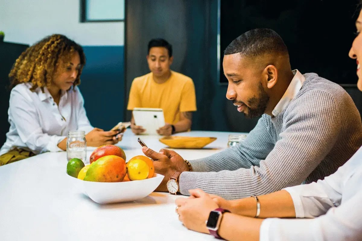 Group of coworkers sitting around a table with fruit bowl during meeting.