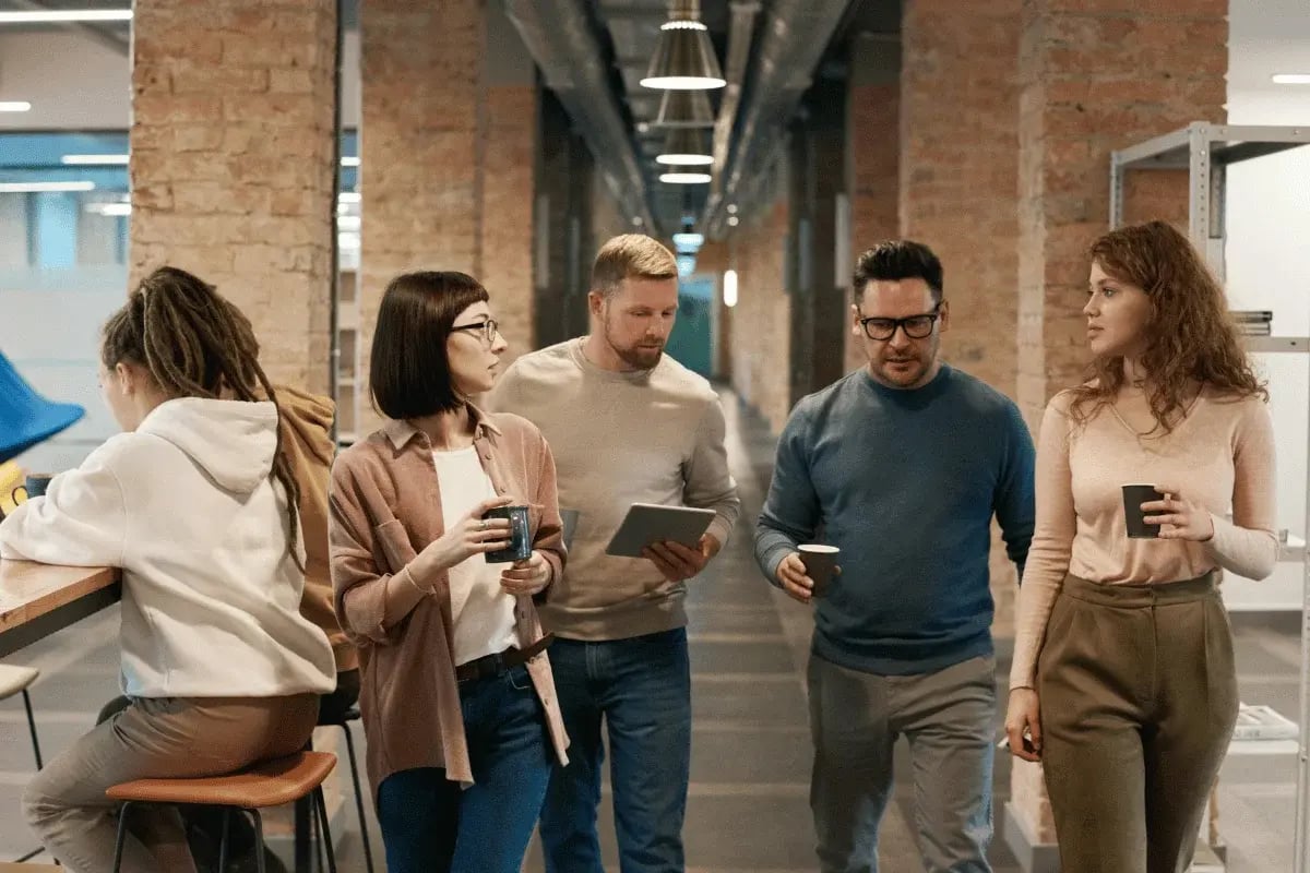 Group of coworkers walking and talking in a modern office hallway.