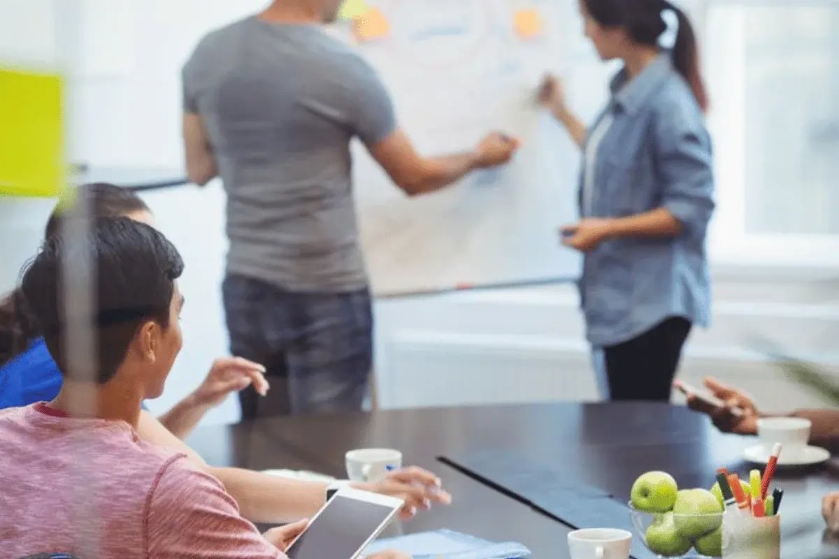 A group of people collaborates in a meeting room, engaging with a presentation on a flip chart, surrounded by stationery and drinks.