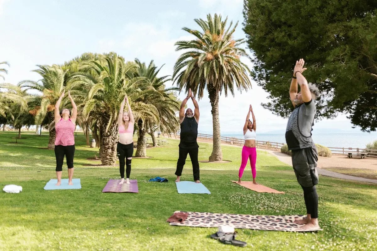 Group of people practicing yoga outdoors on a sunny day in a park.