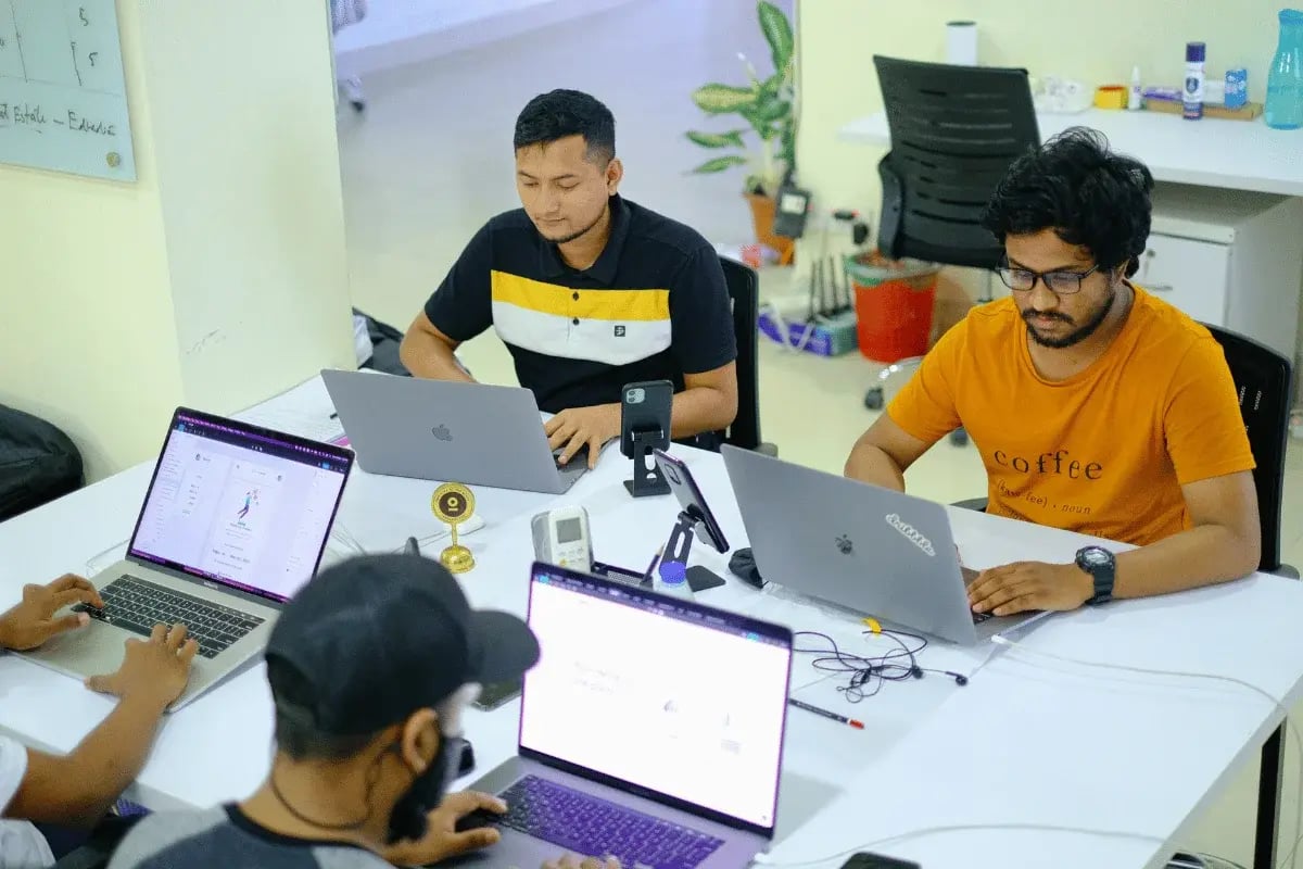 A group of professionals working collaboratively at a modern office desk with MacBook laptops.