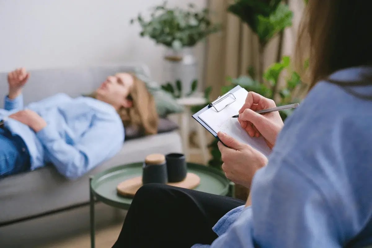 Therapist taking notes while a patient lies on a couch during a counseling session.