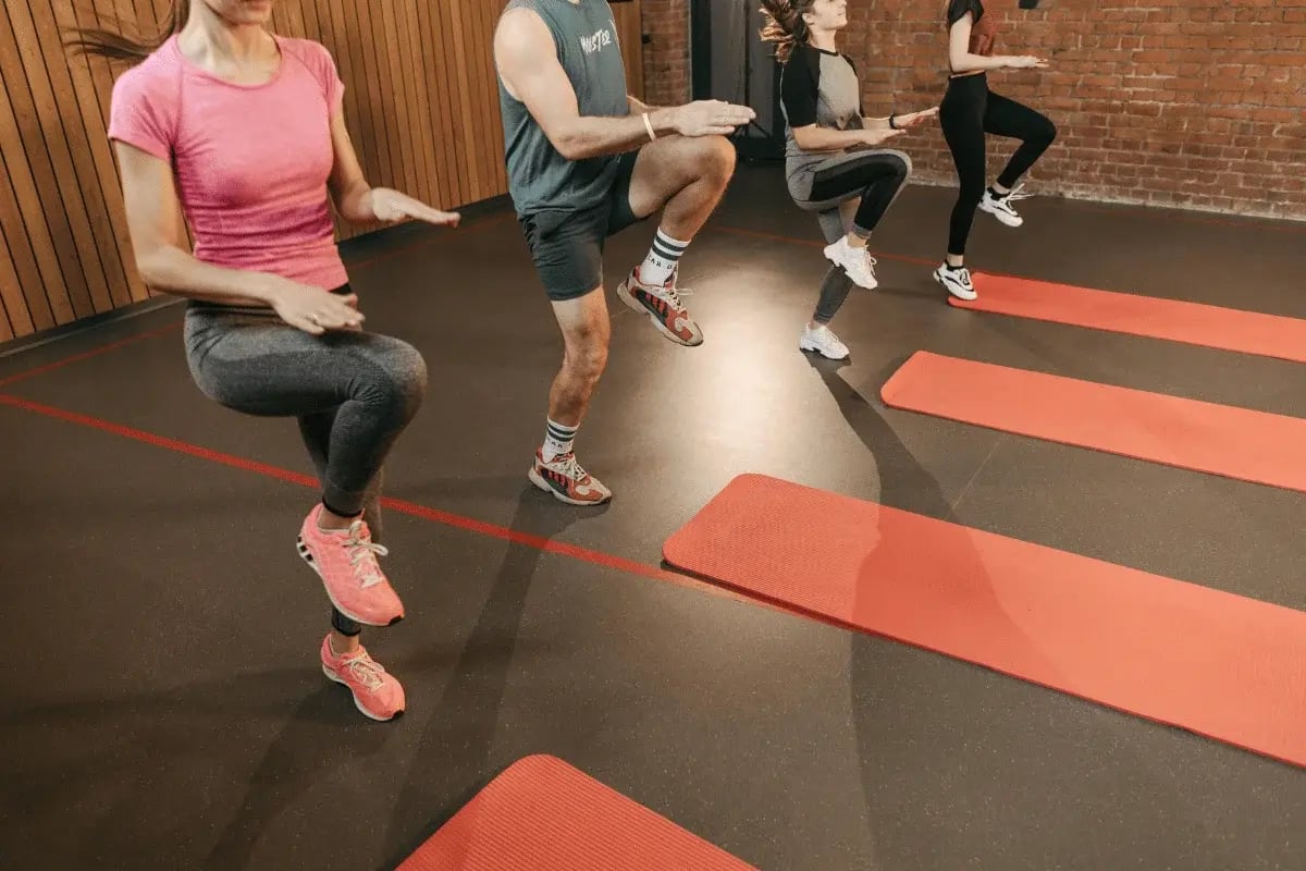 Group fitness class doing high-knee exercises on red mats in an indoor gym with brick walls.