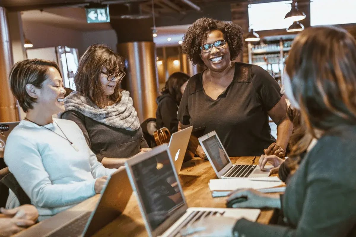 Diverse group of colleagues smiling and collaborating on laptops during a team meeting.