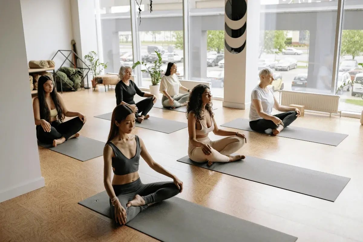 A group of people practicing yoga in a serene studio, sitting cross-legged on mats.