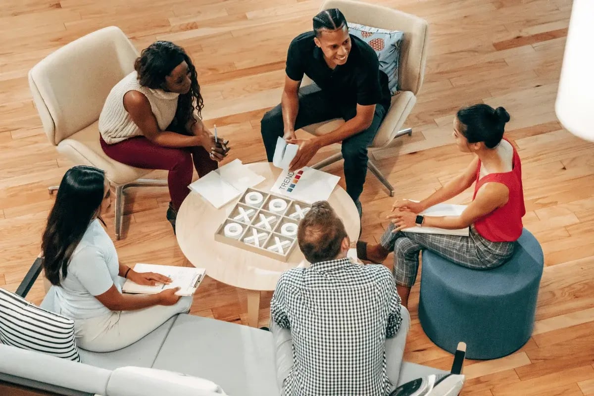 Team of diverse coworkers sitting in a circle discussing documents during a creative office meeting.
