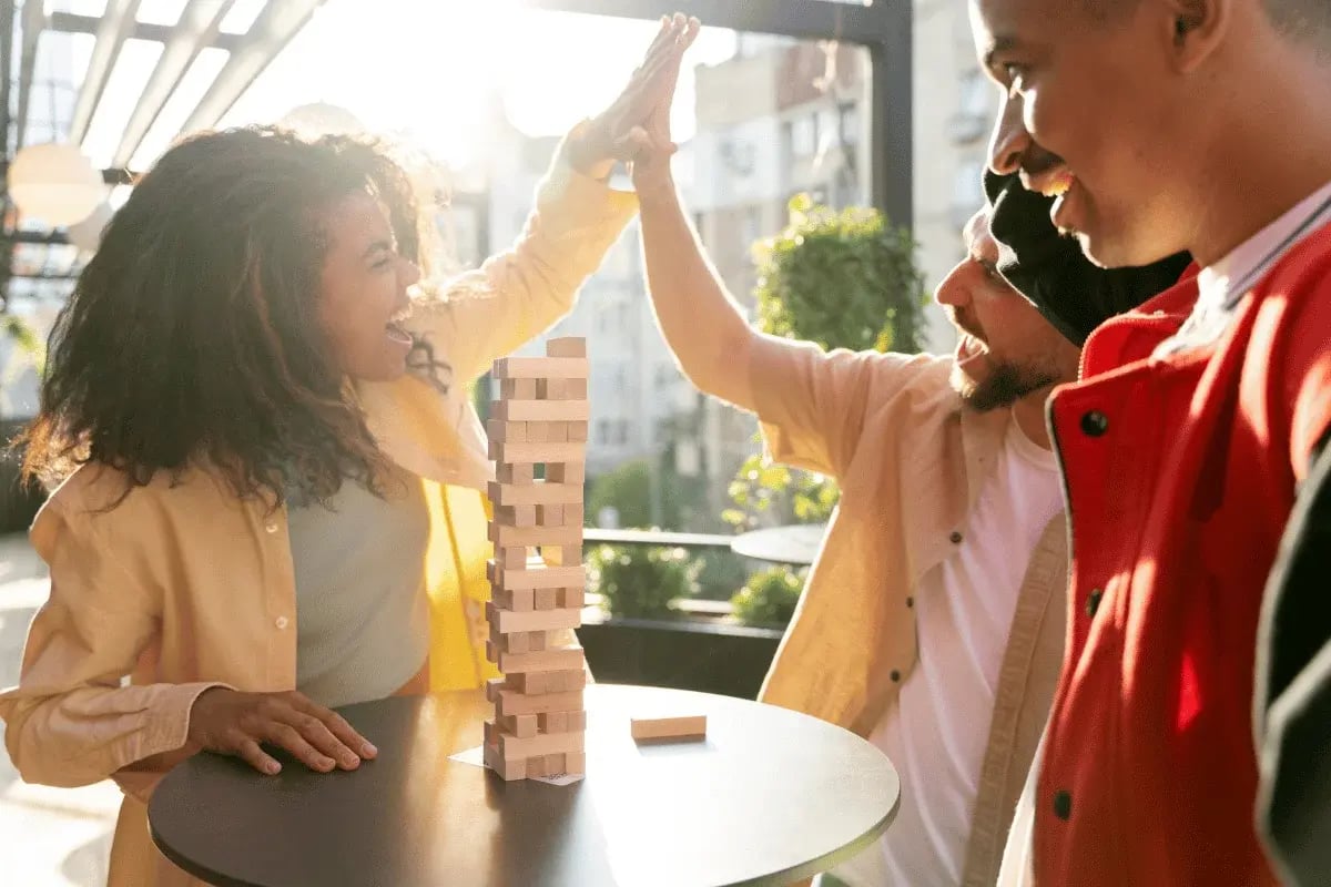 Friends celebrating a Jenga win with a high-five on a sunny patio.