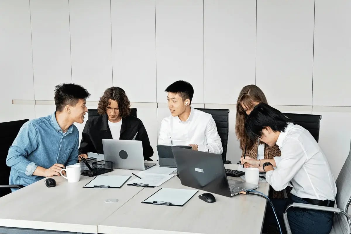 A group of five colleagues collaborates around a conference table, engaging with laptops and documents, fostering a productive and focused atmosphere