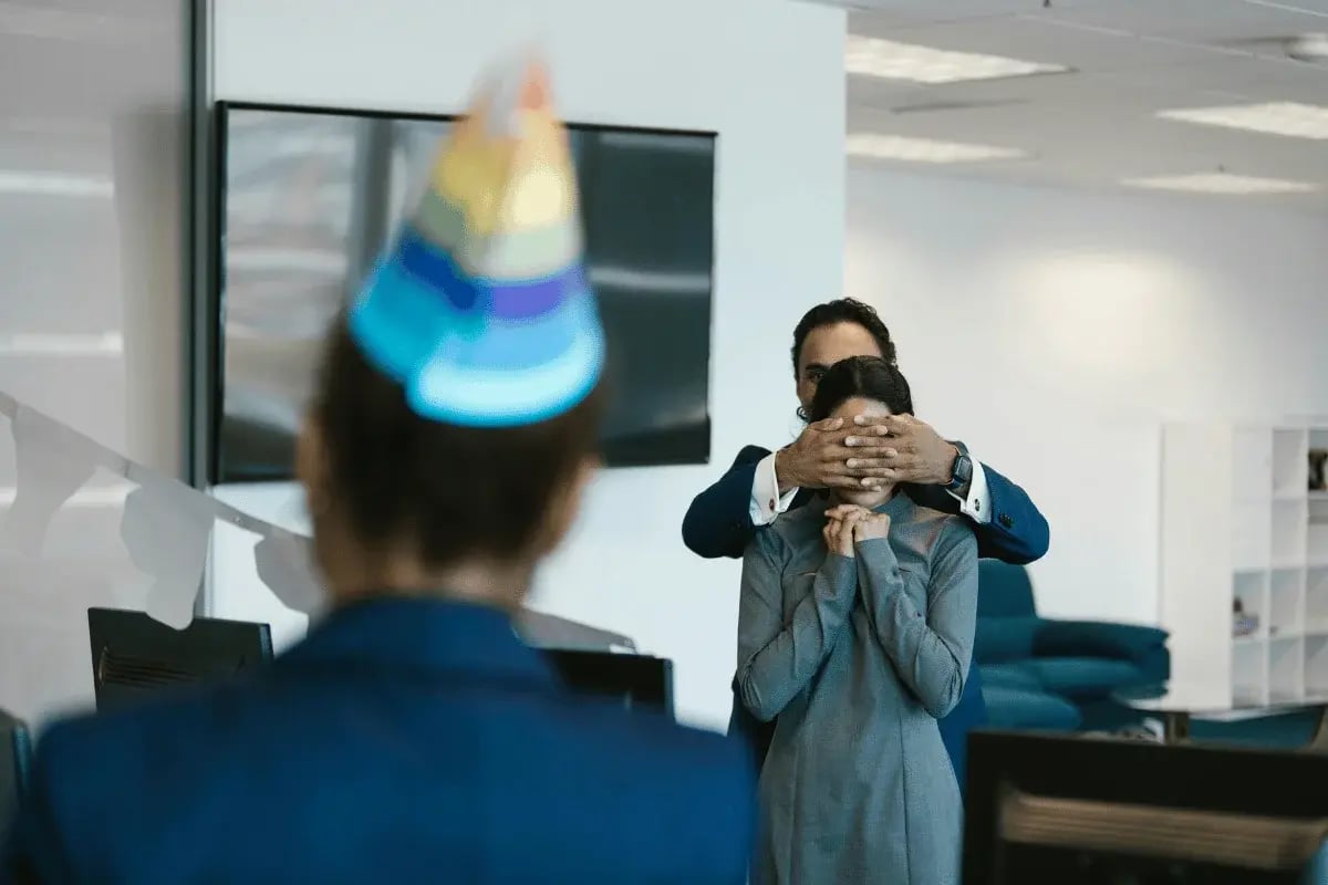 Office worker being surprised with hands over eyes during birthday celebration
