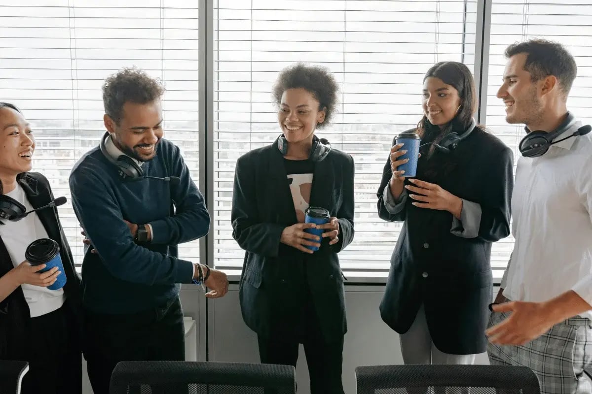 Team of coworkers laughing and enjoying coffee in an office.