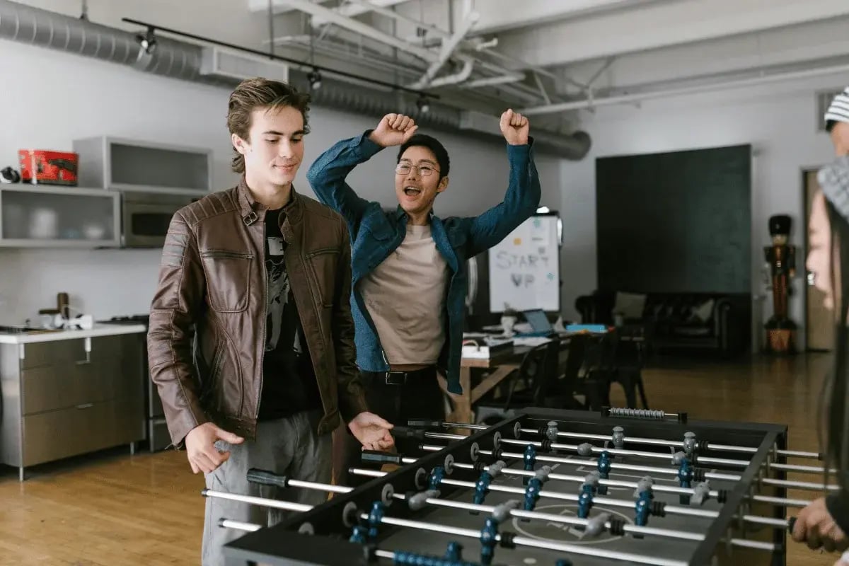 Young professionals playing foosball in a startup office with one celebrating a winning goal.