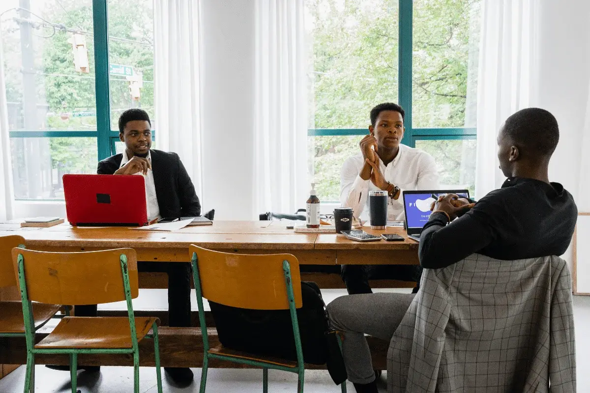 Three businessmen in a modern office discussing work around a long table.