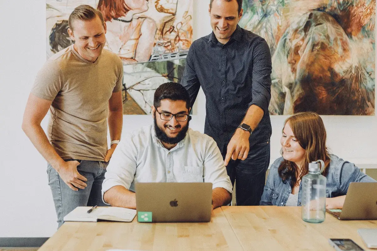 Group of colleagues smiling while collaborating on laptop project.