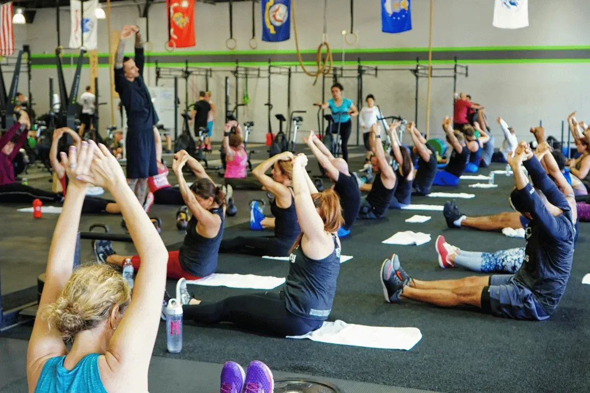 A group of individuals in workout attire perform stretching exercises on mats in a fitness gym, promoting health and wellness.