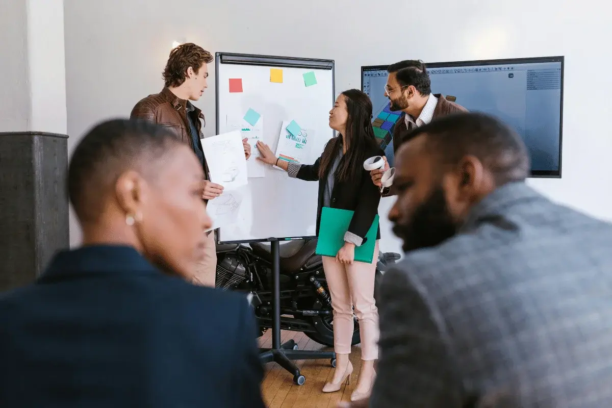A team collaborates around a whiteboard covered with notes and papers. One person gestures, while others listen intently, creating an engaged and focused atmosphere.