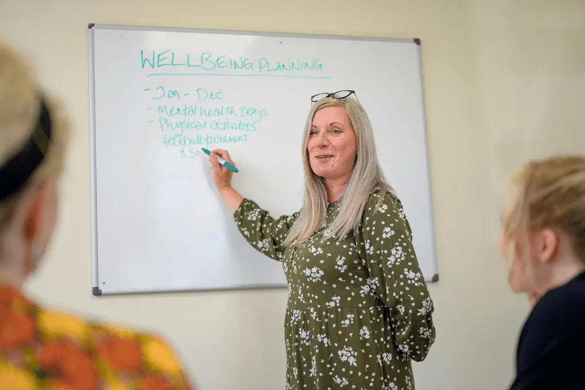 A woman in a green floral dress stands by a whiteboard labeled 